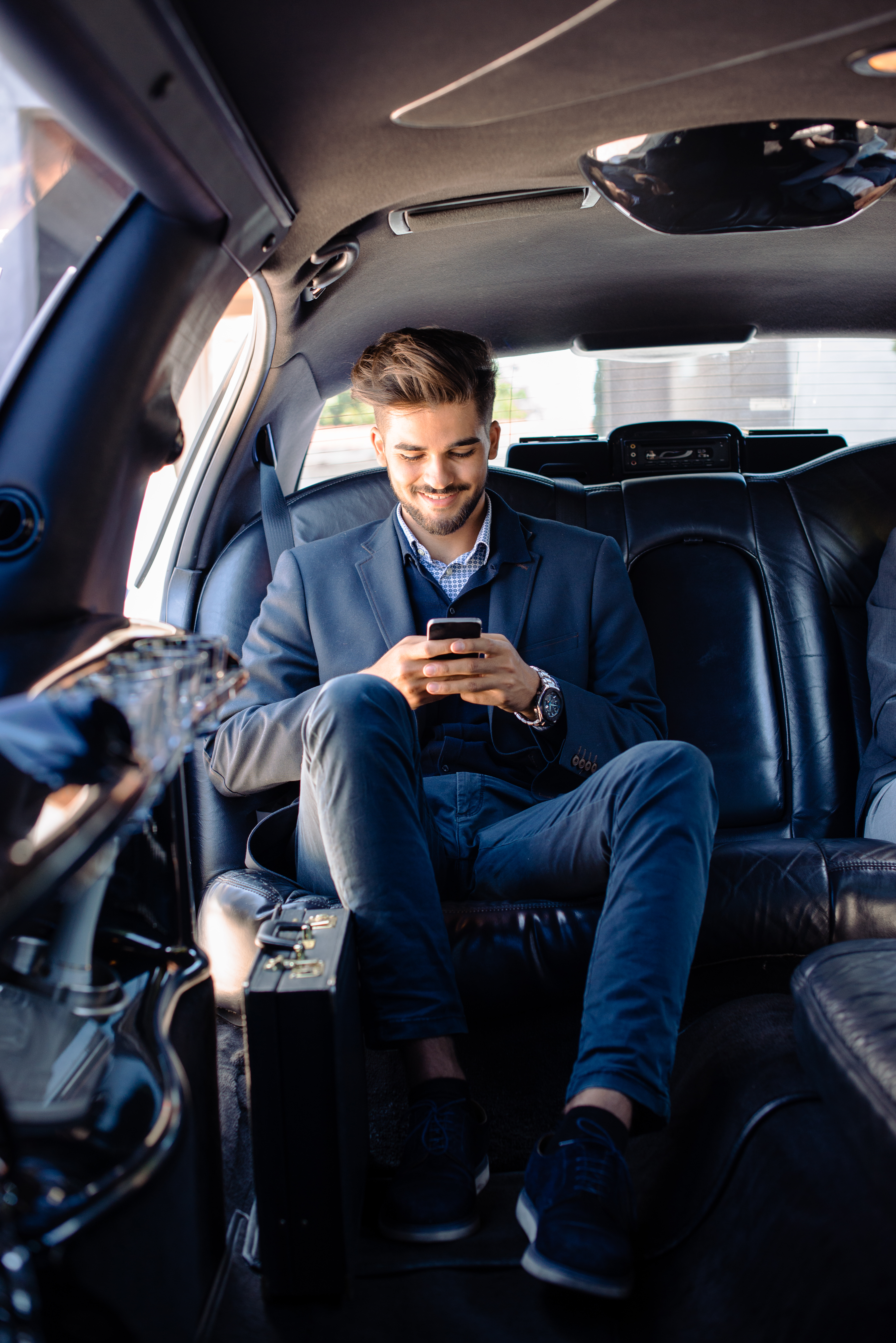 A smiling chauffeur stands next to a black vehicle.